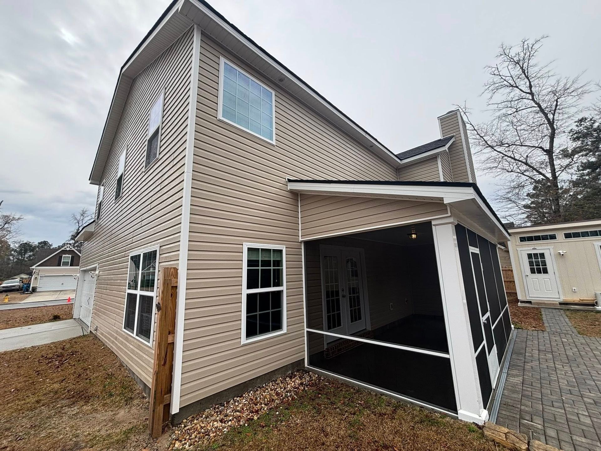 A beige two-story house with a screened-in porch and a stone walkway in a yard on an overcast day.