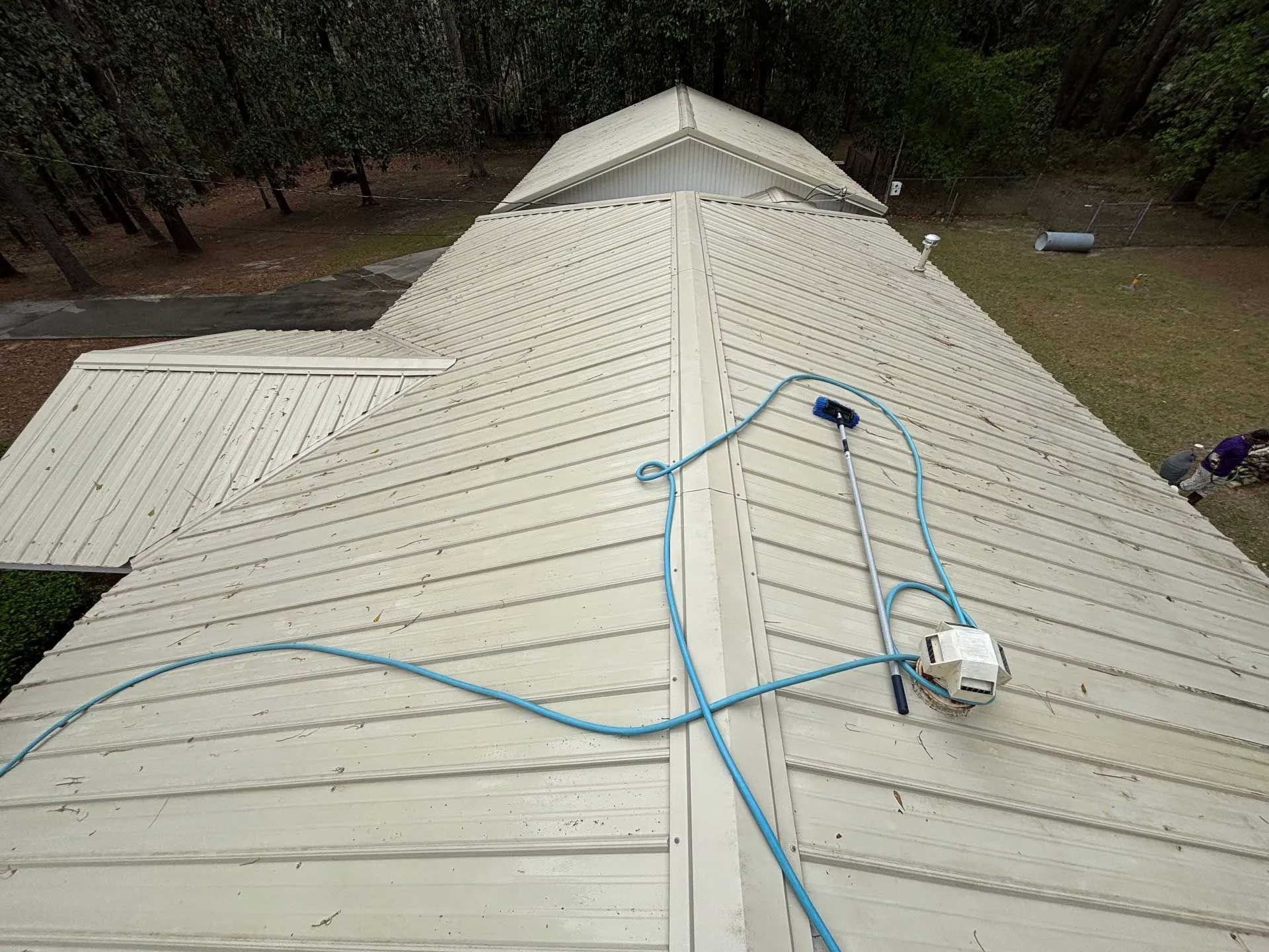 A metal roof being cleaned with a pressure washer; blue hose and machine on the roof.