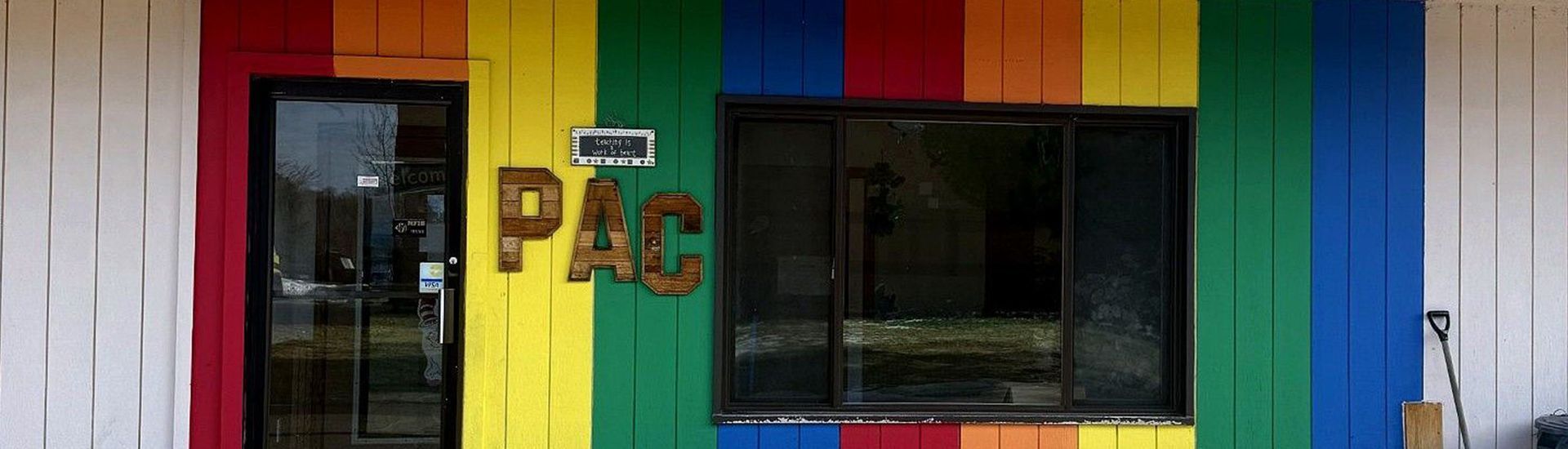 Building exterior with a rainbow-colored facade, featuring a door, large window, and the letters PAC.