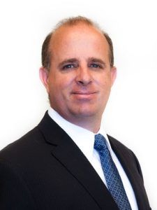 Portrait of a man in a dark suit with a blue tie against a white background
