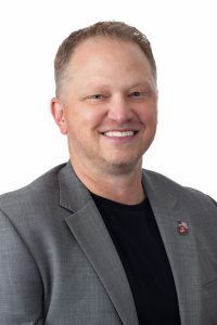 Smiling man in a gray blazer and black shirt against a white background