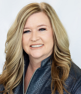 Smiling woman with long blonde hair wearing a dark blue jacket on a light background