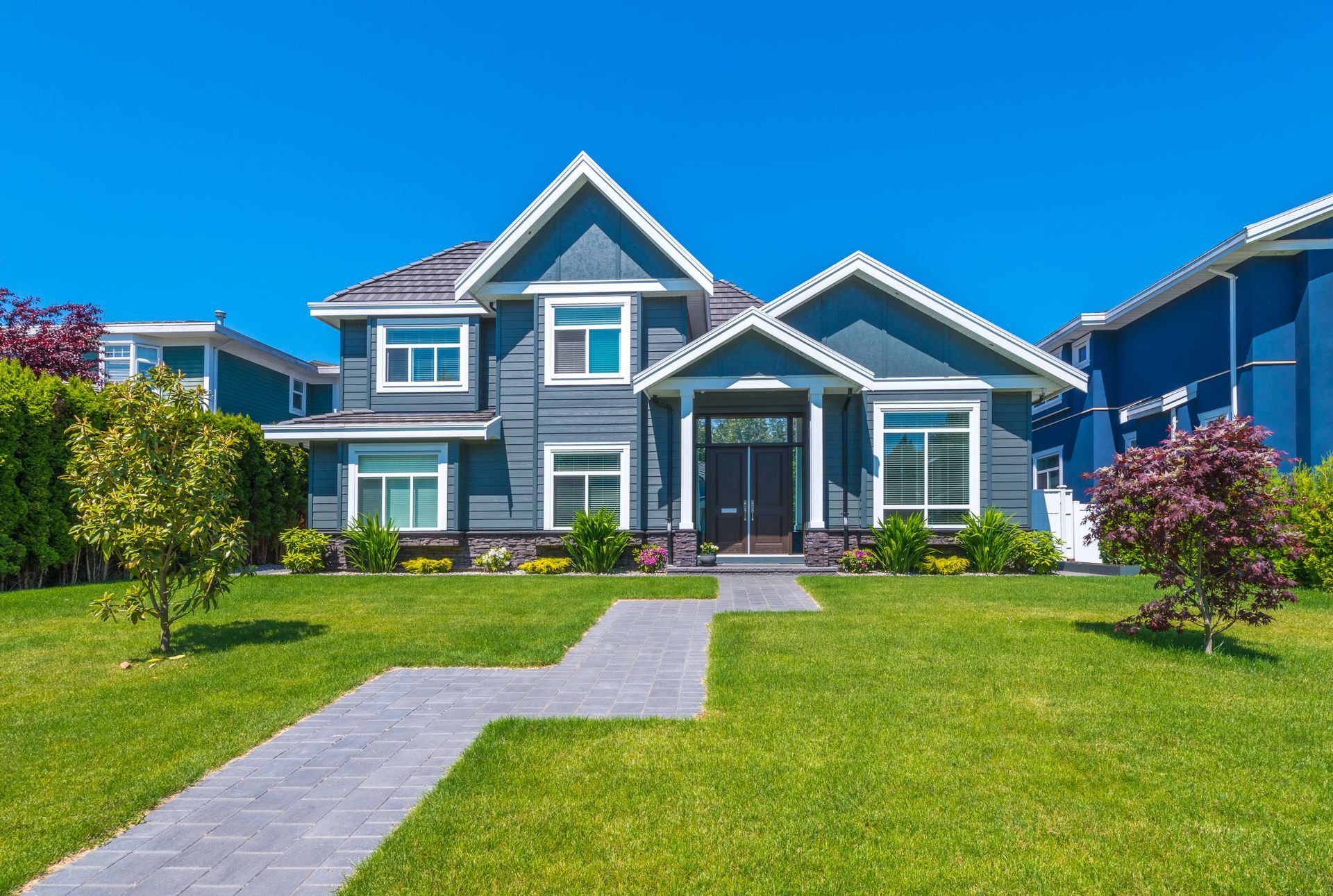 Blue suburban house with manicured lawn and a stone walkway under a clear sky
