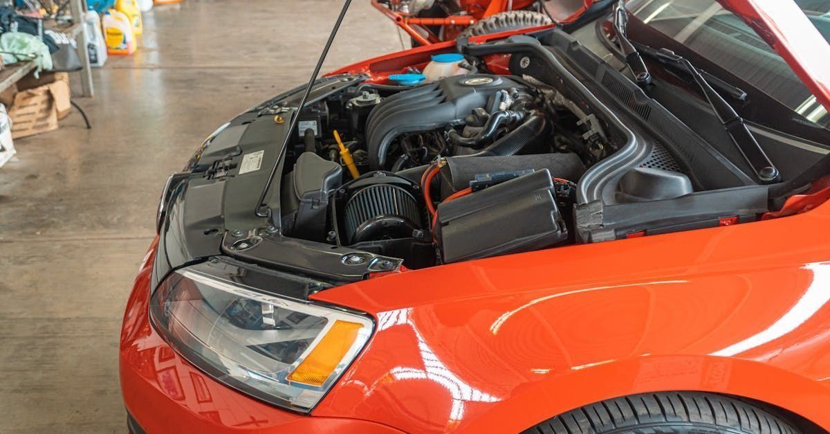 Red car with its hood open, showing the engine compartment in a garage.