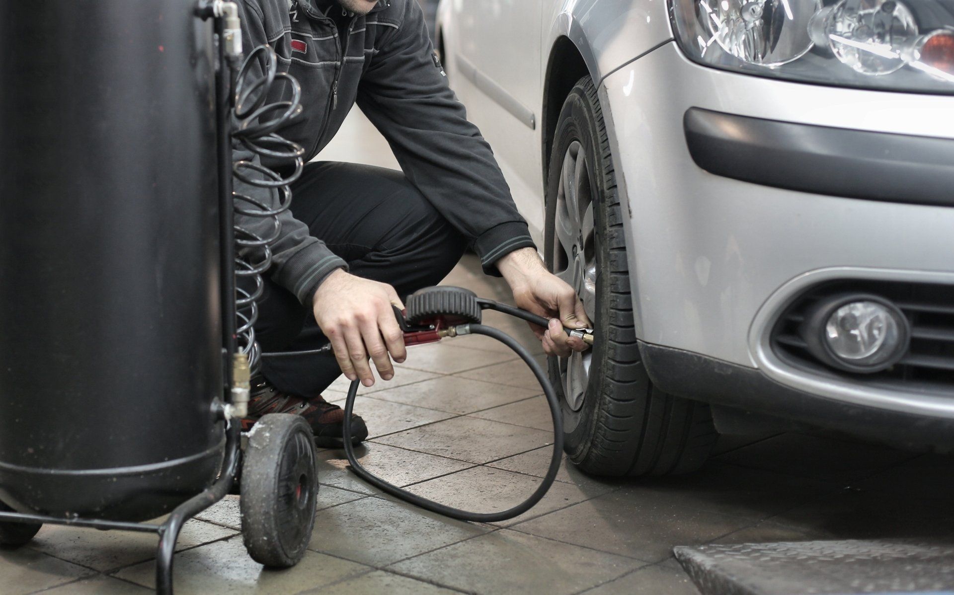 Mechanic attaching a tire inflator to a car’s front wheel beside a silver vehicle