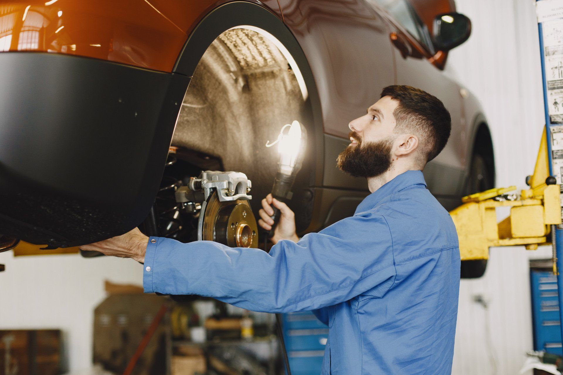 Mechanic in blue shirt inspecting a car’s raised front wheel in an auto repair shop