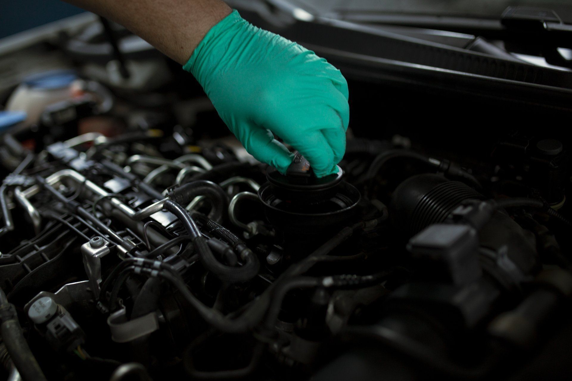 Gloved hand inspecting car engine components under the hood