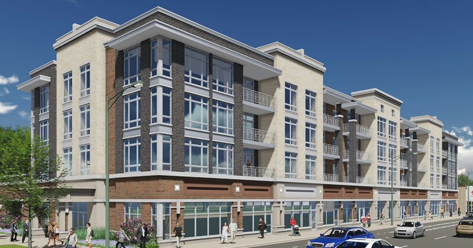Street corner with red-brick apartment building, large windows, trees, and a few pedestrians under a blue sky