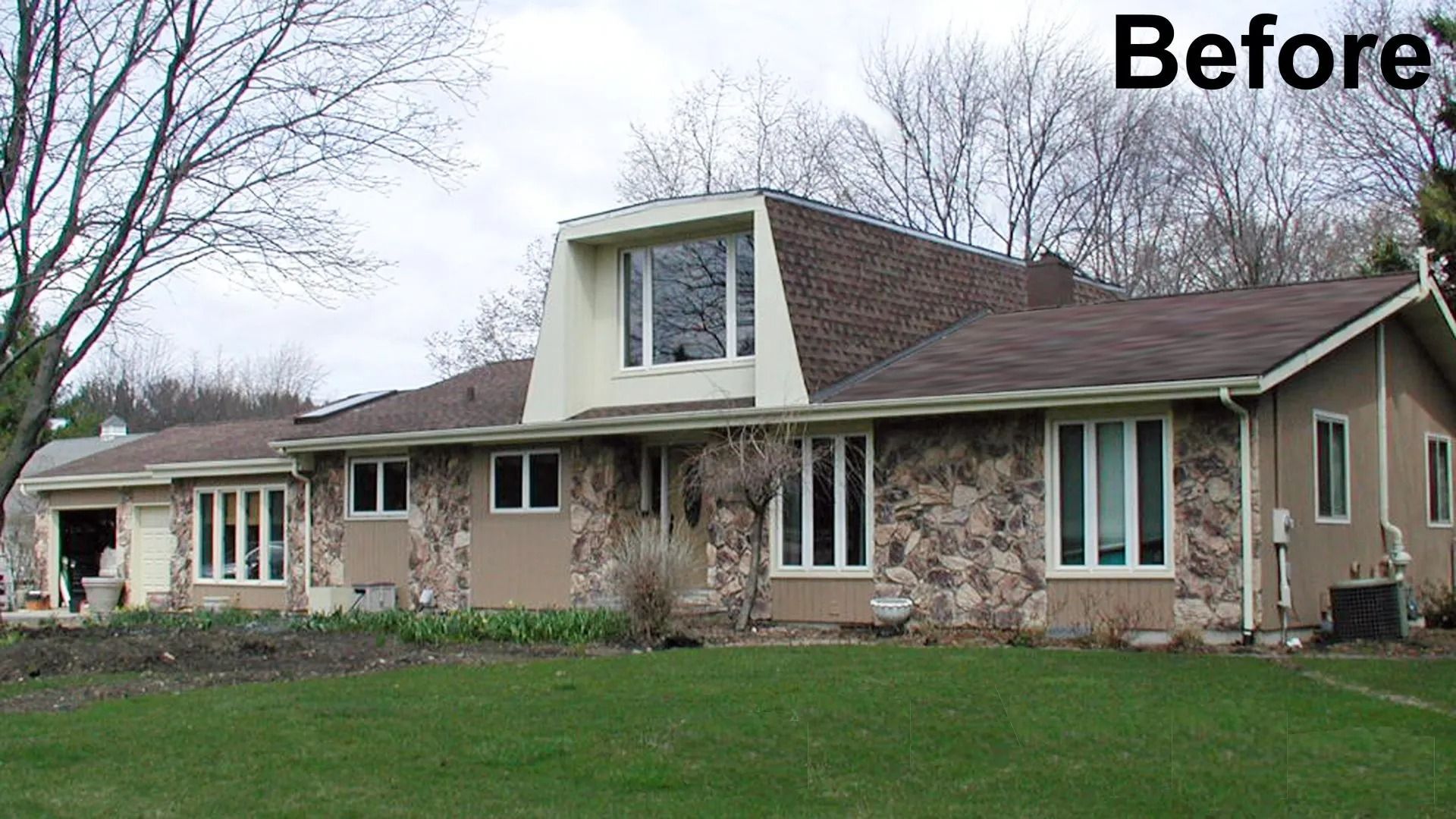 Before view of a single-story stone house with dormer and front lawn