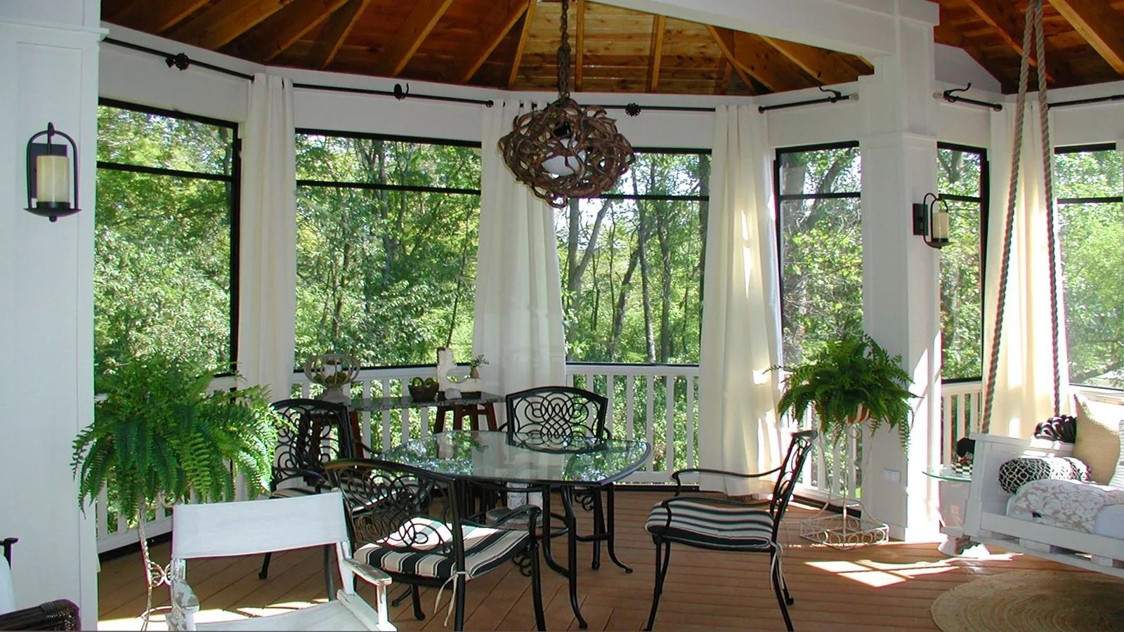 Sunlit indoor sunroom with wicker chairs, large windows, potted plants, and a round table