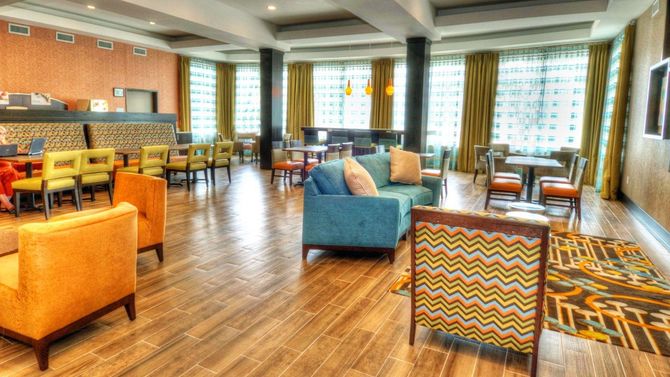 Bright hotel lounge with colorful armchairs, wooden floors, tables, and large windows.