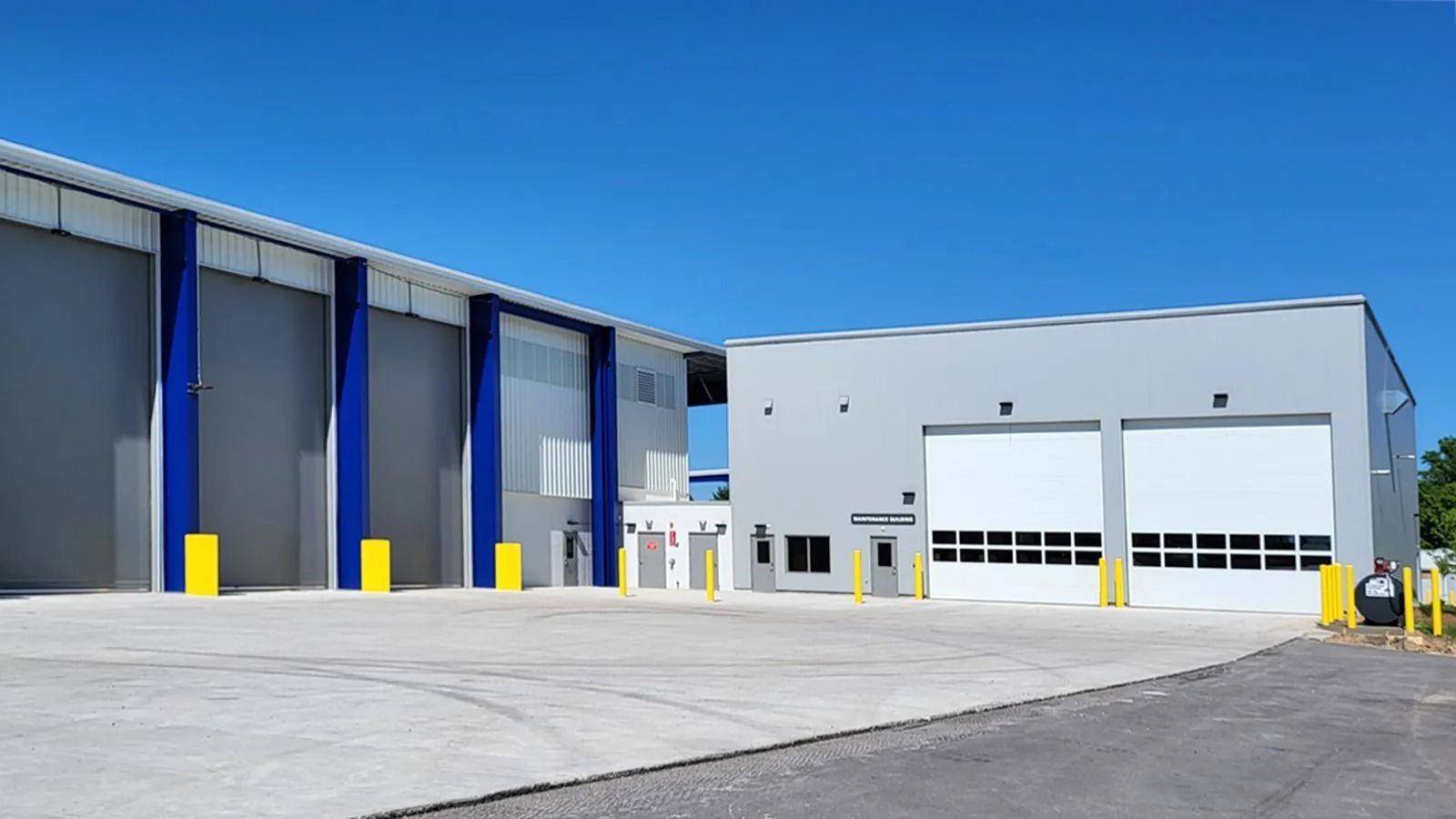 Modern industrial warehouse exterior with blue accents and large garage doors under a clear sky