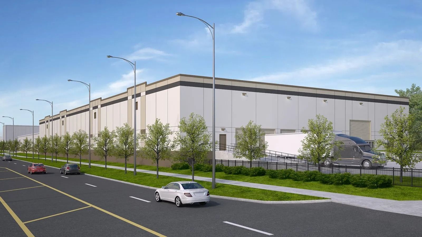 Large beige industrial warehouse beside a road, with cars, streetlights, and trees under a clear sky