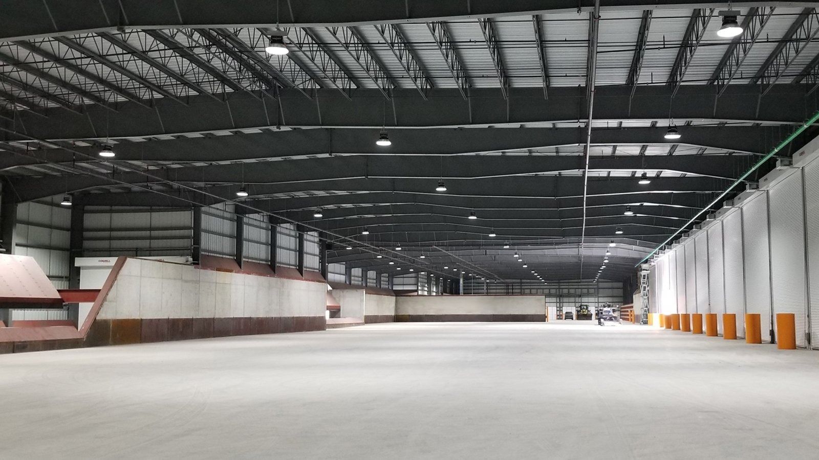 Empty warehouse interior with high metal roof and concrete floor, lit by skylights.