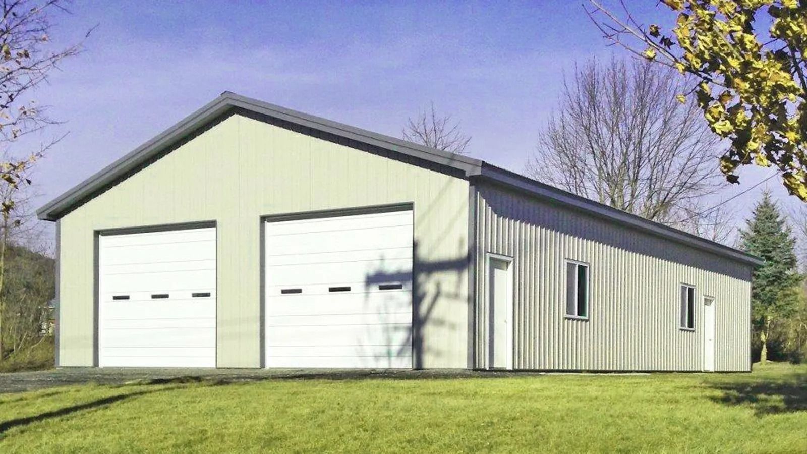 White two-bay garage with a dark roof on a grassy lot under a clear blue sky