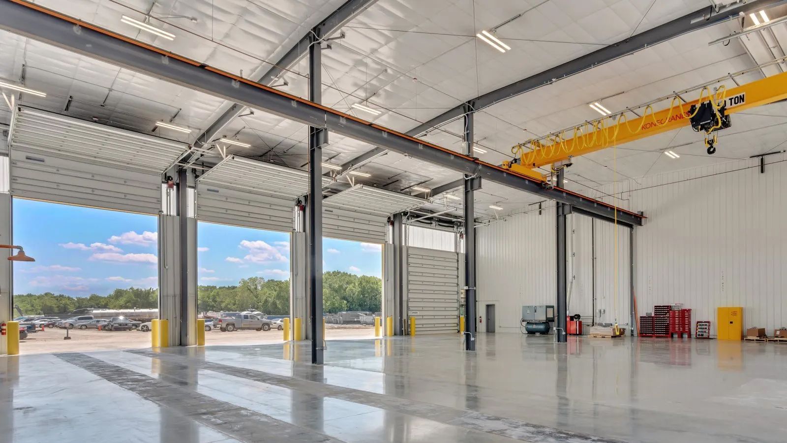 Empty industrial warehouse with high ceilings, open bay doors, and a yellow overhead crane