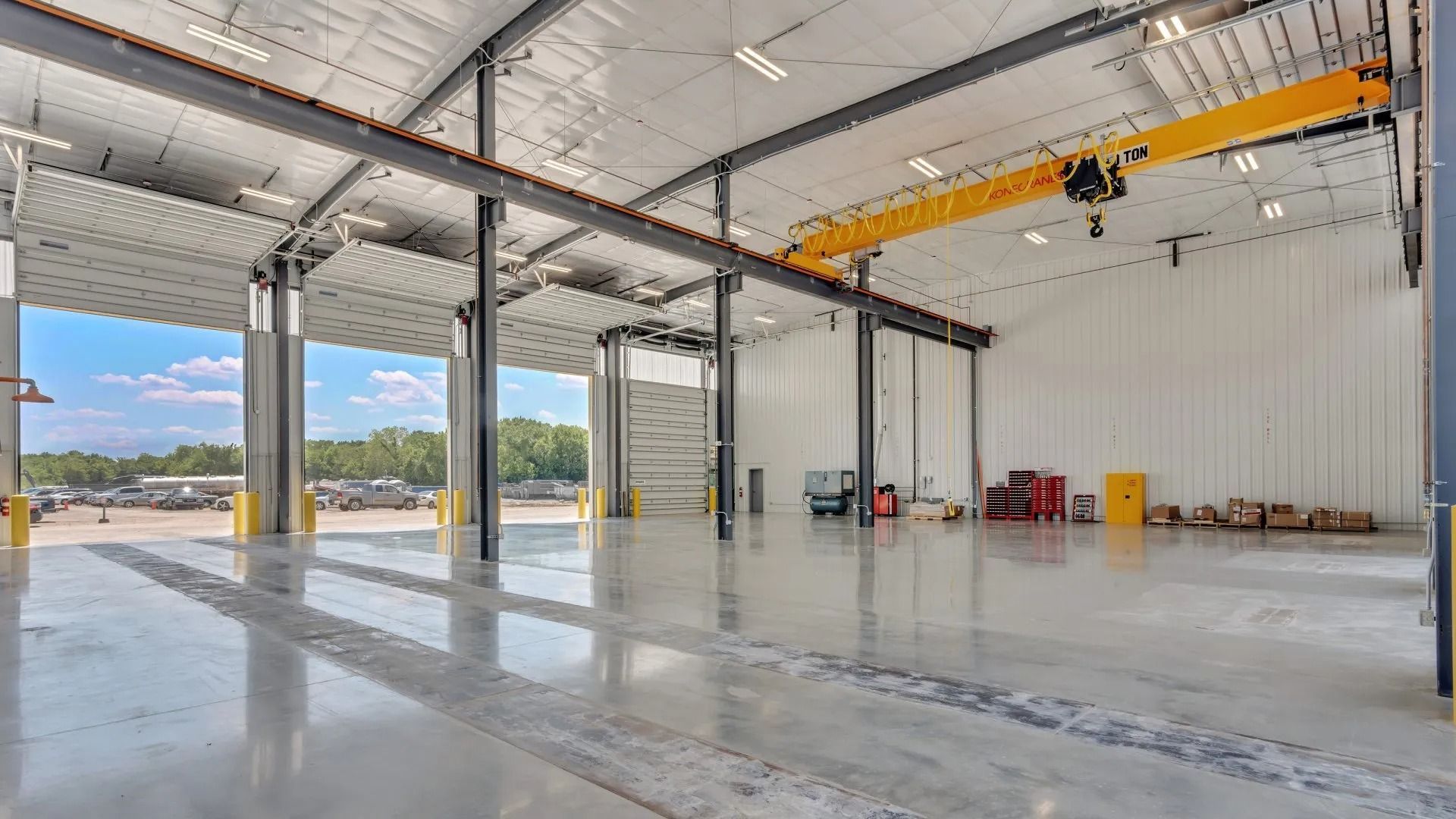 Empty industrial warehouse with high ceiling, yellow overhead crane, and open bays letting in daylight