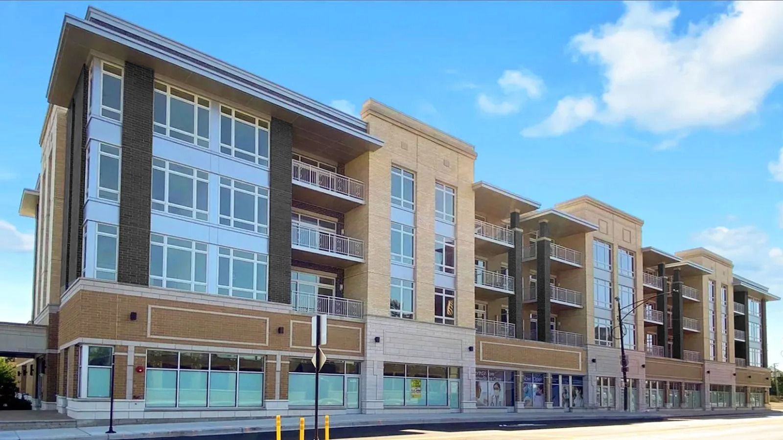 Modern multi-story apartment building with brick and glass storefronts along a sunny street