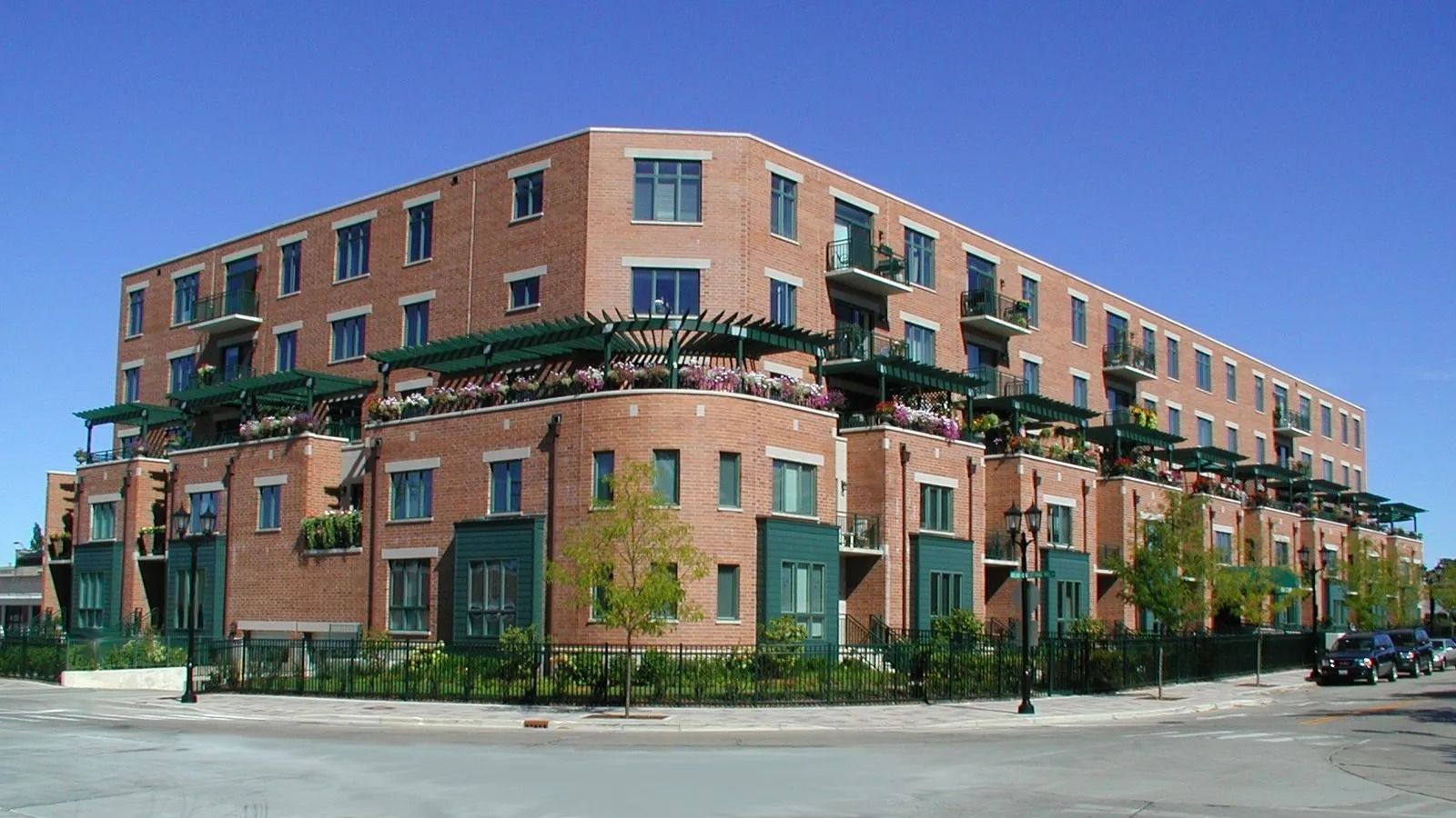 Brick apartment building with green balconies on a street corner under a clear sky