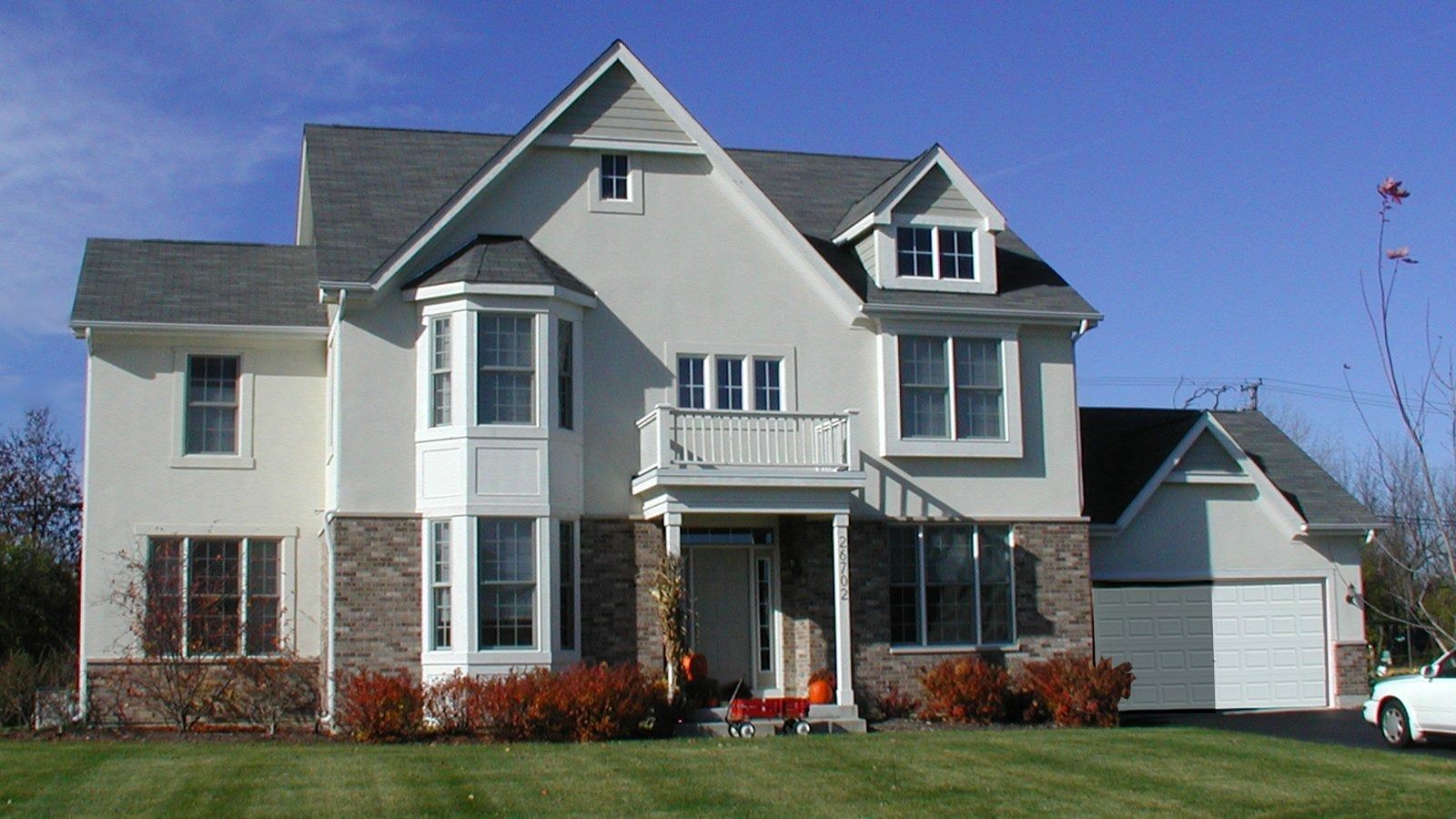 Large gray two-story suburban house with white trim, front porch, and a detached garage under a clear blue sky