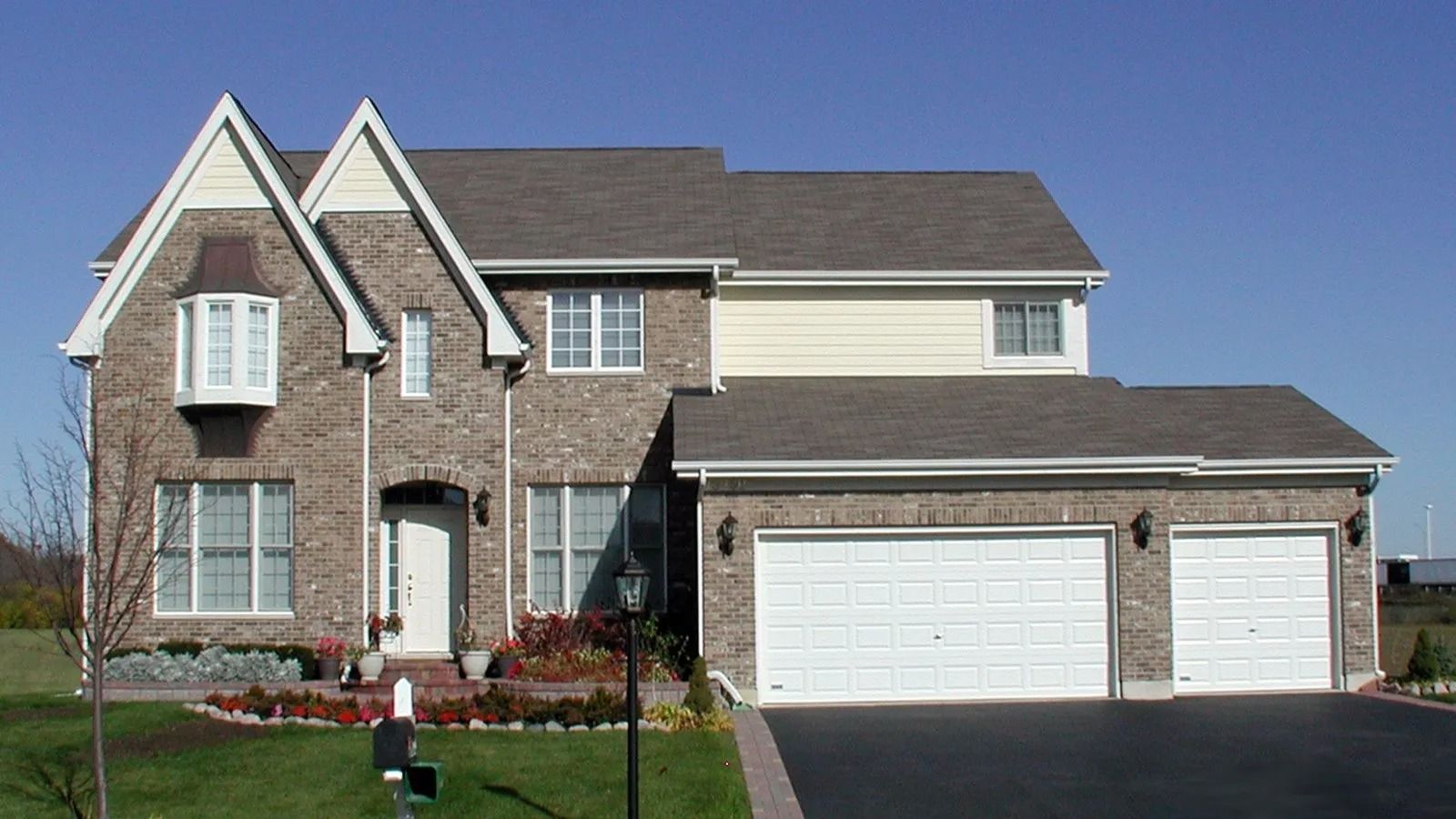 Two-story brick suburban house with attached two-car garage and a manicured front lawn