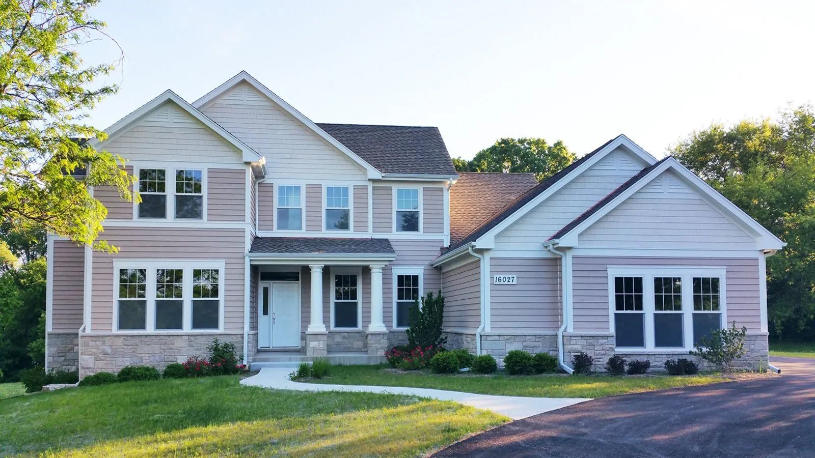 Two-story white suburban house with black roof, front porch, and manicured lawn in daylight