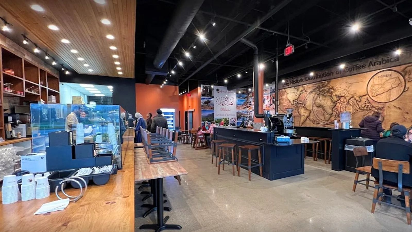 Modern coffee shop interior with tables, stools, counter, and warm wood and black decor