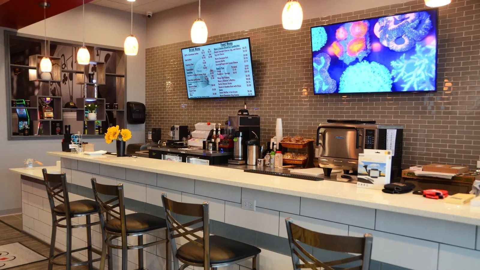 Modern café counter with stools, brick wall, pendant lights, and two wall-mounted menu screens