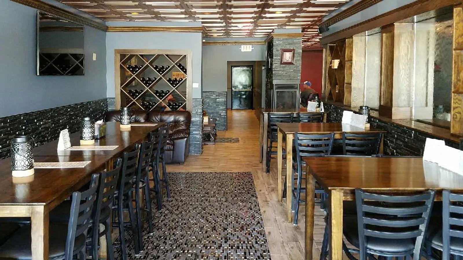 Empty restaurant dining room with wooden tables, black chairs, and a patterned tile floor.