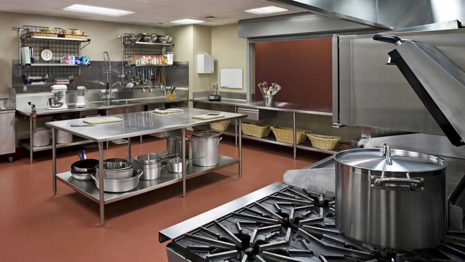 Commercial kitchen with stainless steel counters, stovetop, and large pots under bright lights