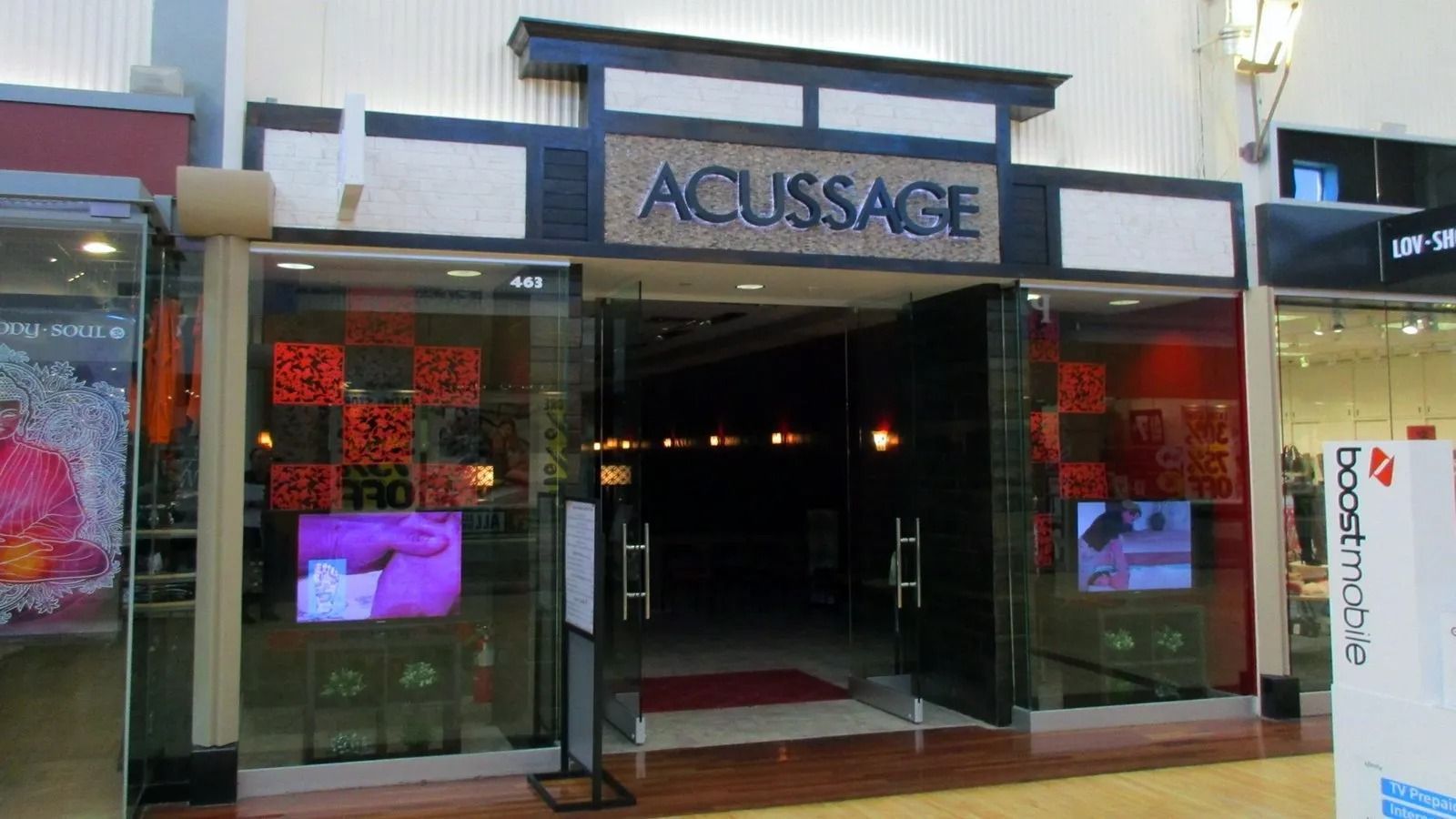 Storefront entrance with a sign reading “ACUSSAGE,” flanked by colorful display windows.
