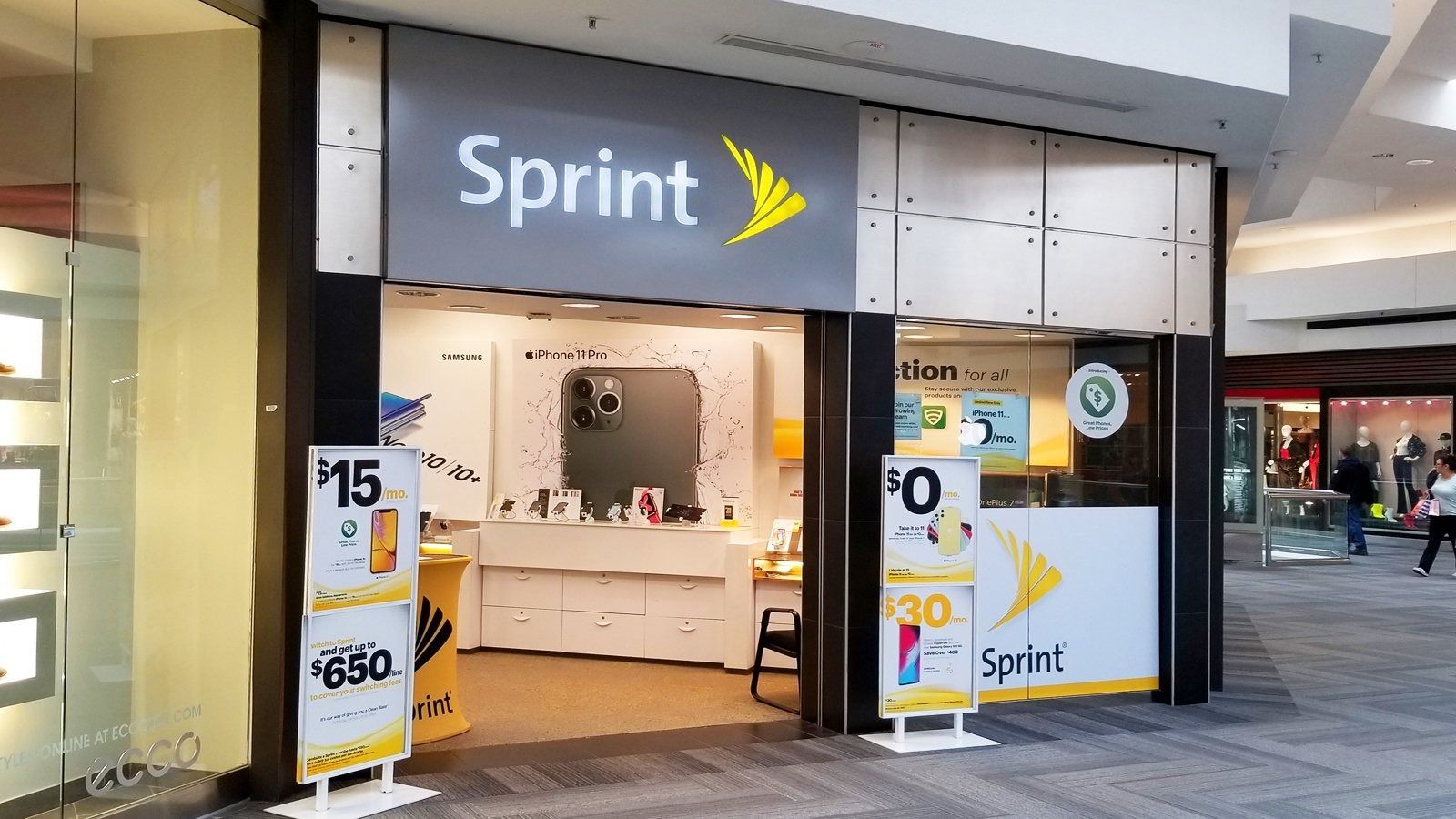 Sprint store entrance in a mall, with white and yellow signage and phone promo displays
