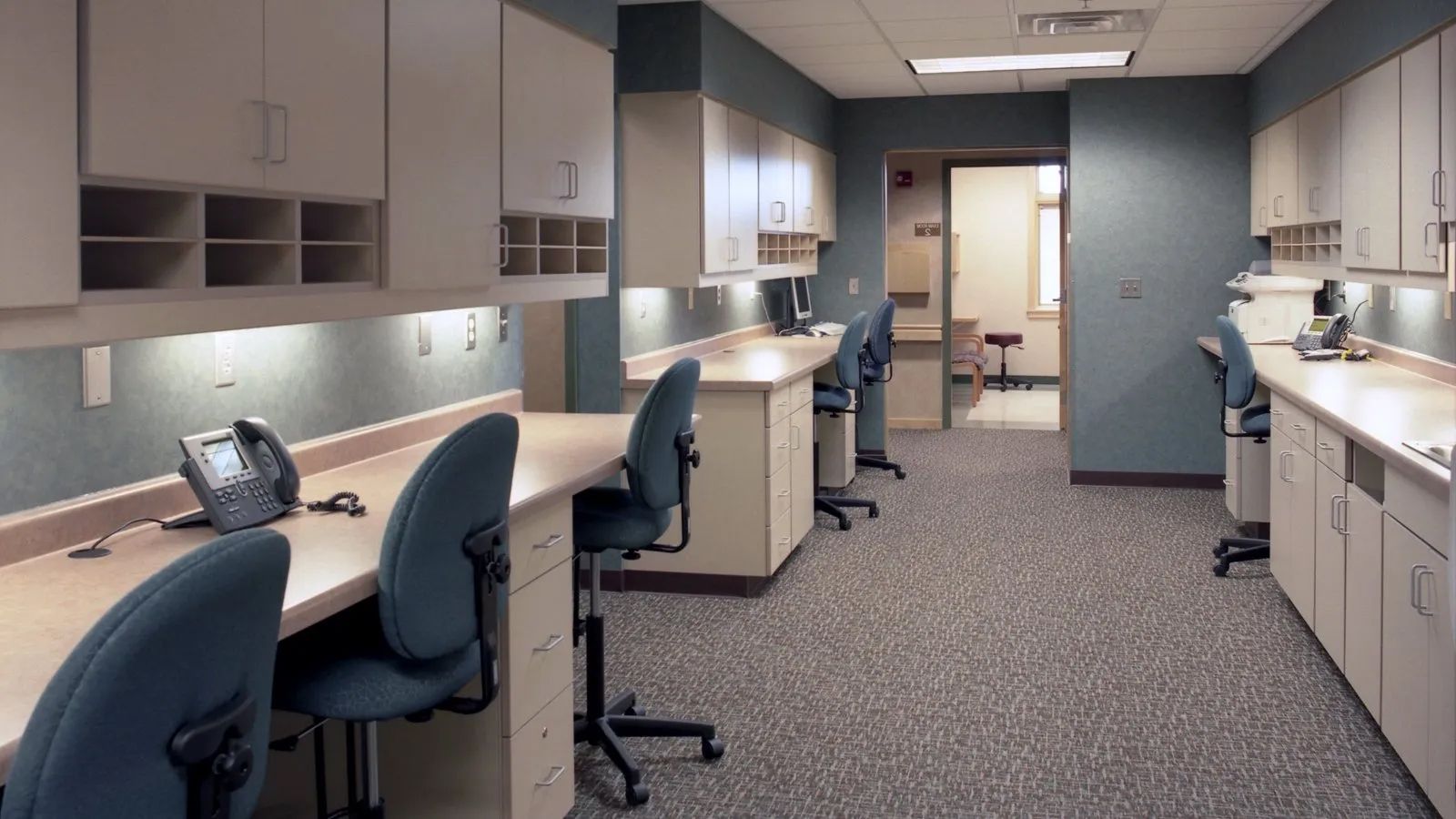 Empty reception desk with curved counters, swivel chairs, monitors, and warm wood-paneled walls in a modern office
