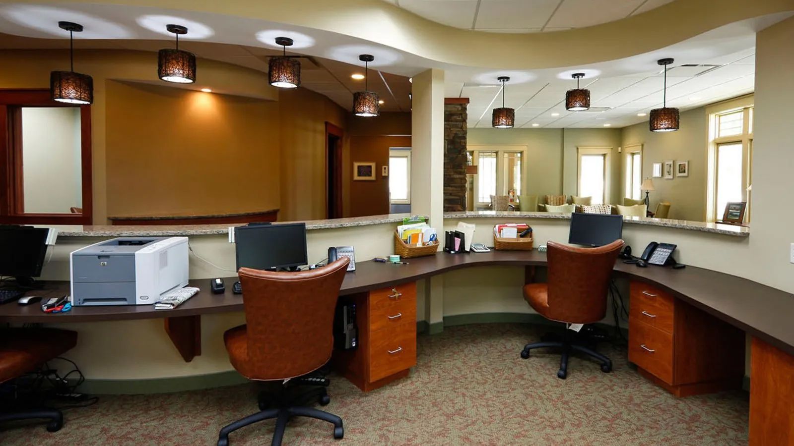 Empty modern reception desk with curved counters, orange chairs, and wall mirrors under warm ceiling lights