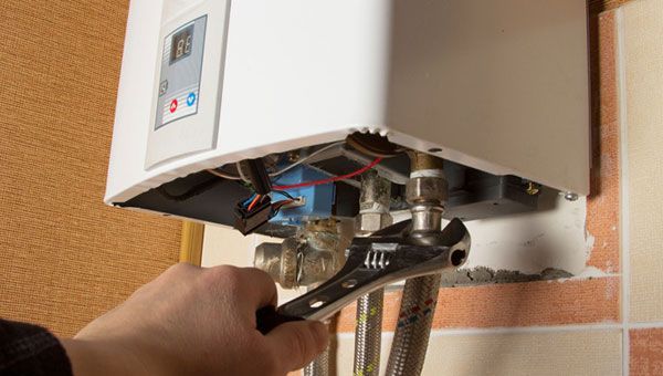 A person is fixing a water heater with a wrench