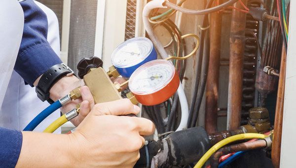 A man is working on an air conditioner with gauges.