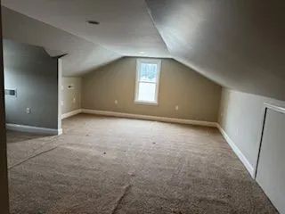 attic room with beige walls and worn brown carpet
