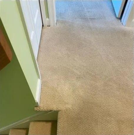 repaired tan carpet by the stairs, next to a green wall and doorway