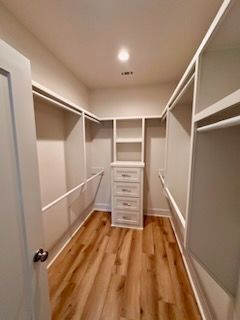 a walk in closet with hardwood floors and white shelves