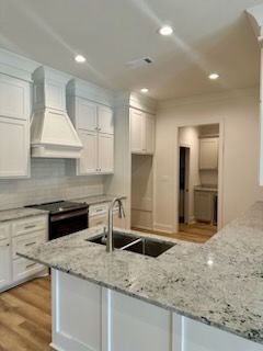a kitchen with white cabinets , granite counter tops , a sink , and a stove