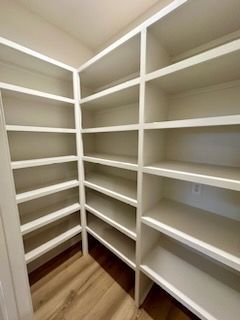 a walk in closet with lots of shelves and wooden floors