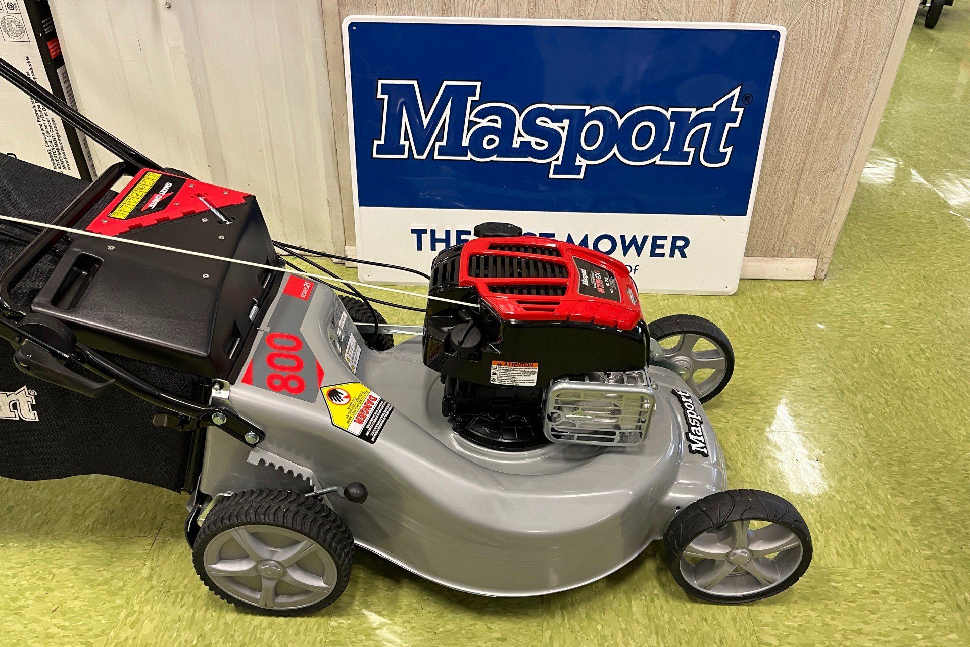 A lawn mower is sitting in front of a Masport sign