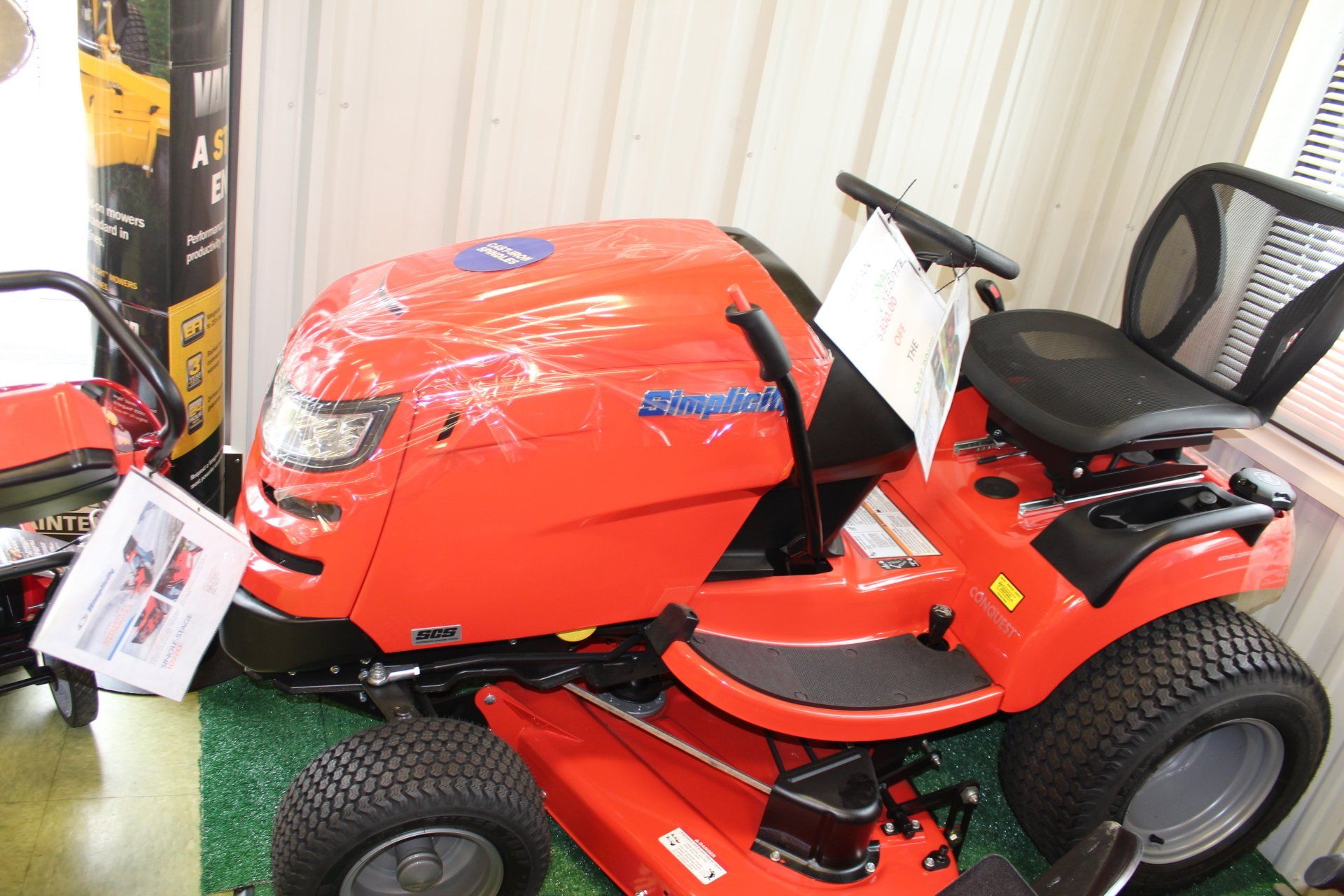 Orange Simplicity riding lawn mower displayed on fake green grass.