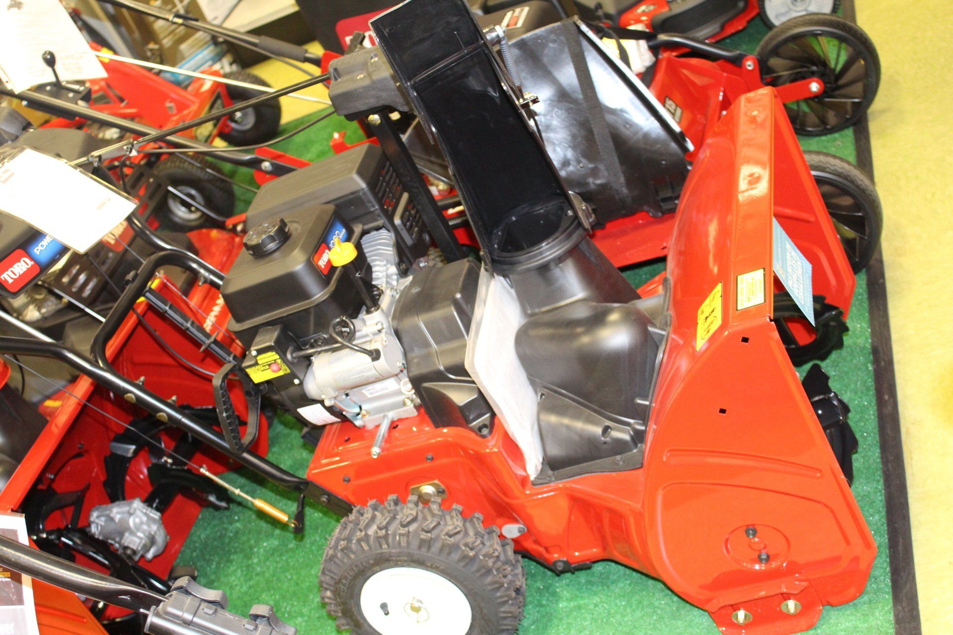 A row of red Toro snow blowers parked on a green display floor.