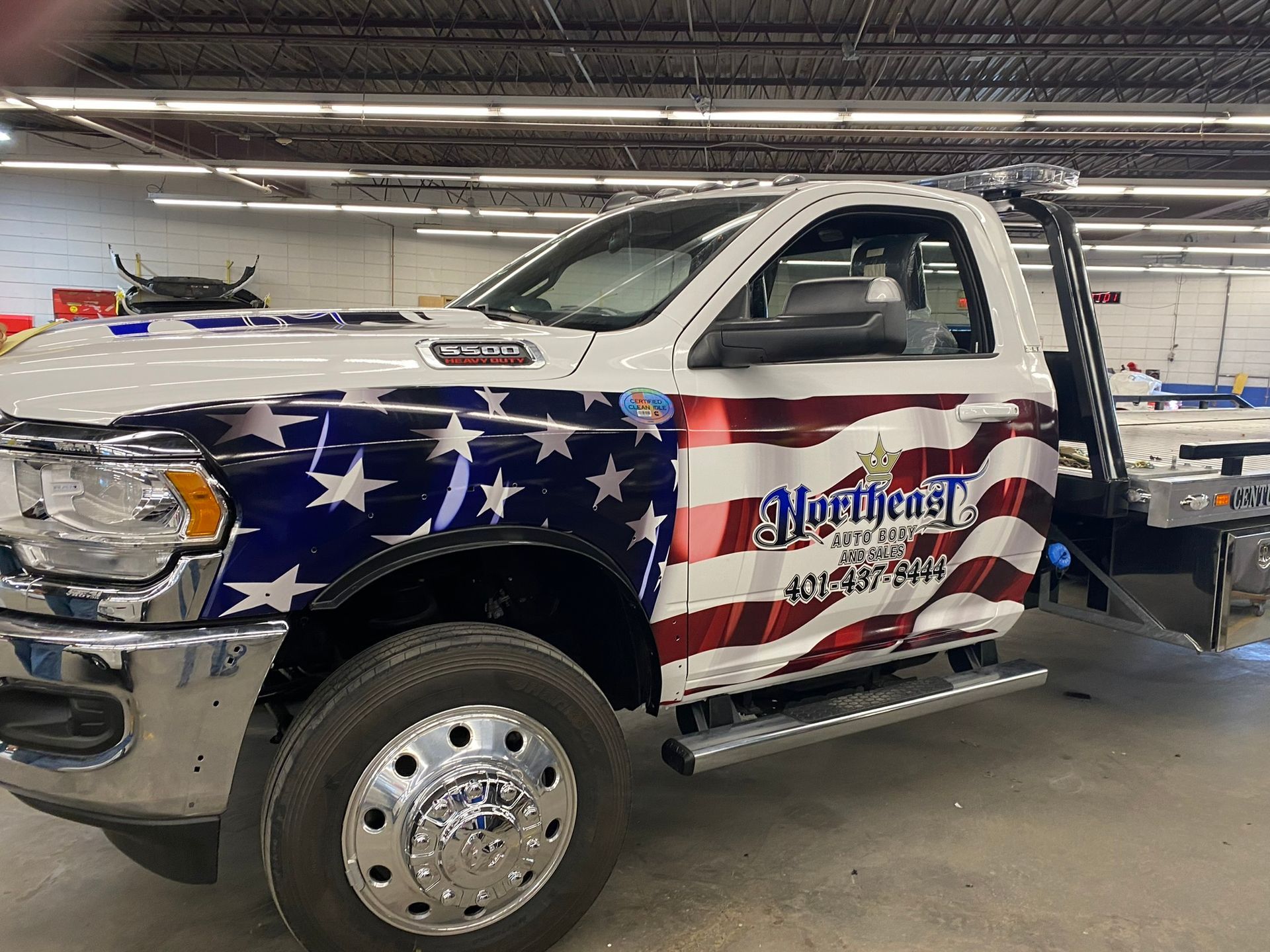 A white tow truck with an american flag wrap is parked in a garage.