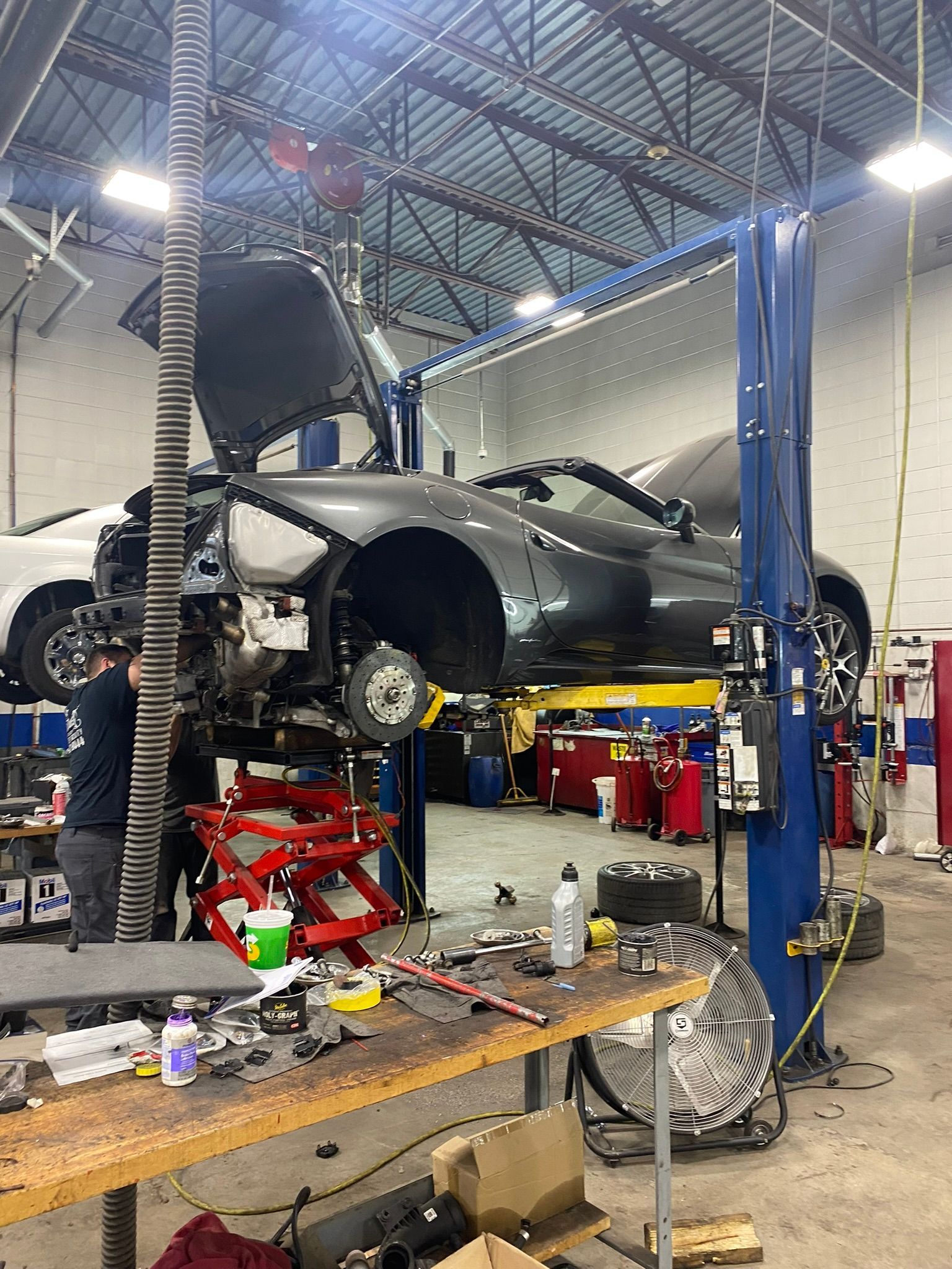 A car is being repaired in a garage with the hood up.