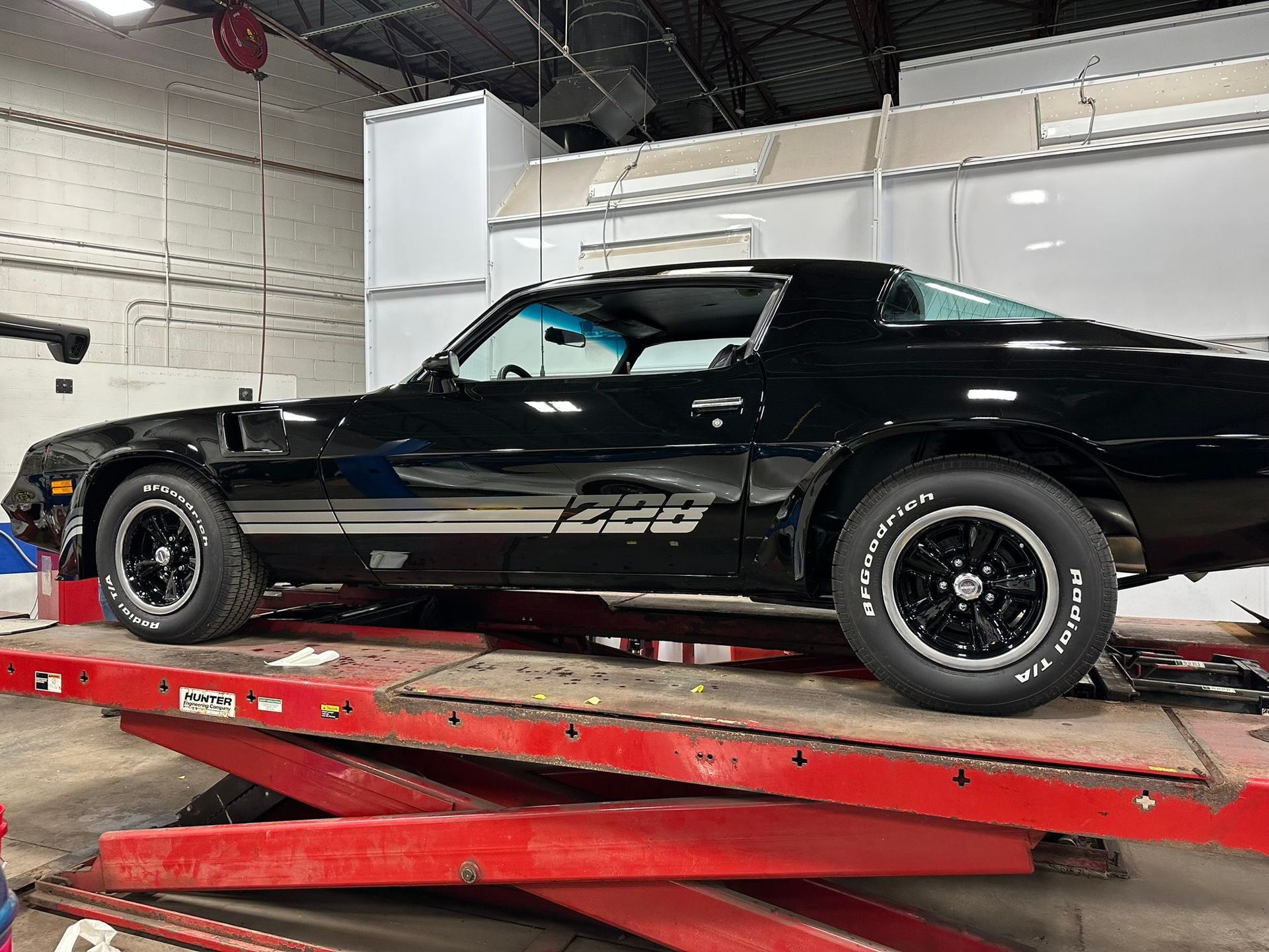 A black car is sitting on top of a red lift in a garage.