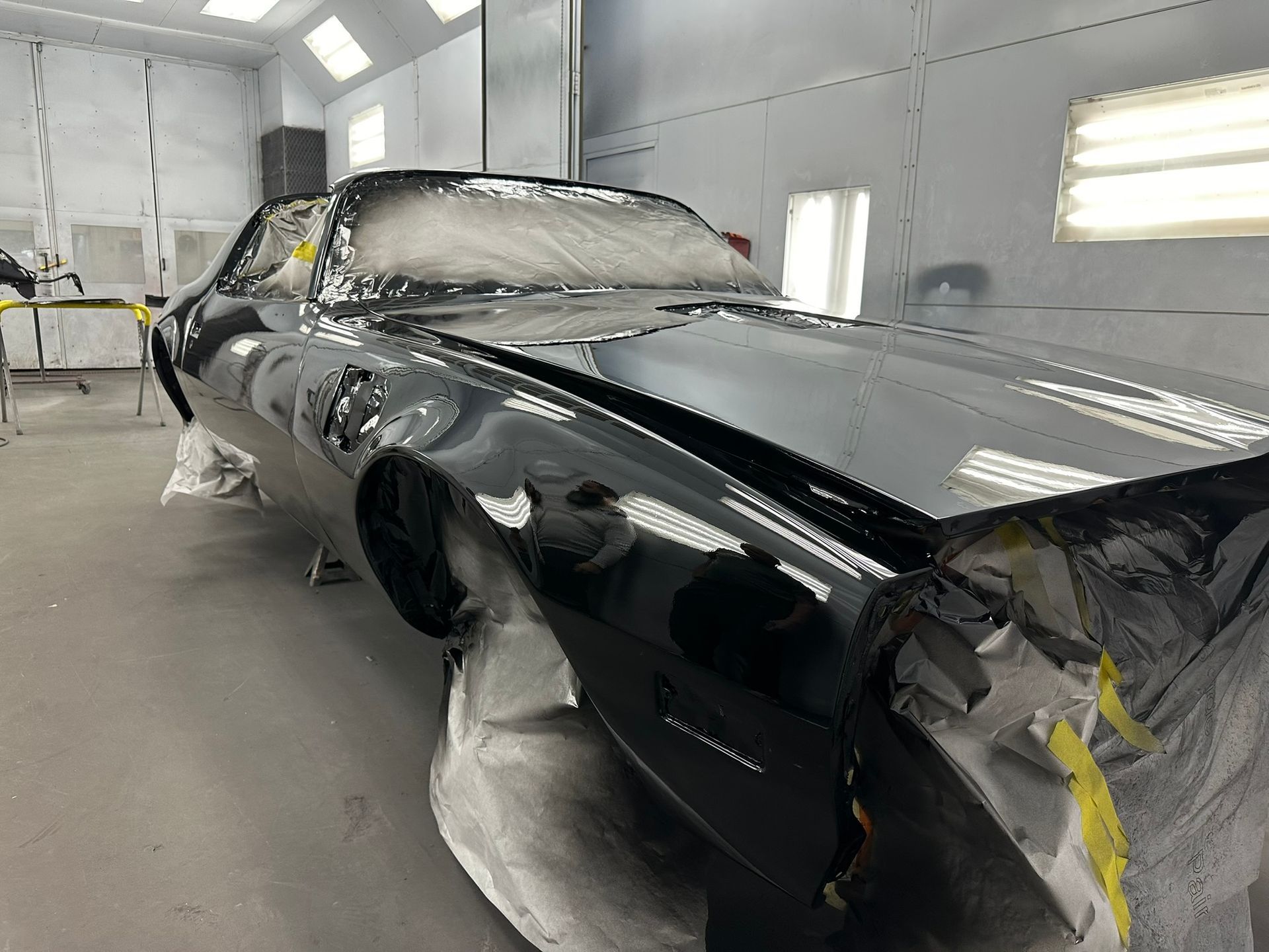 A black car is being painted in a paint booth.