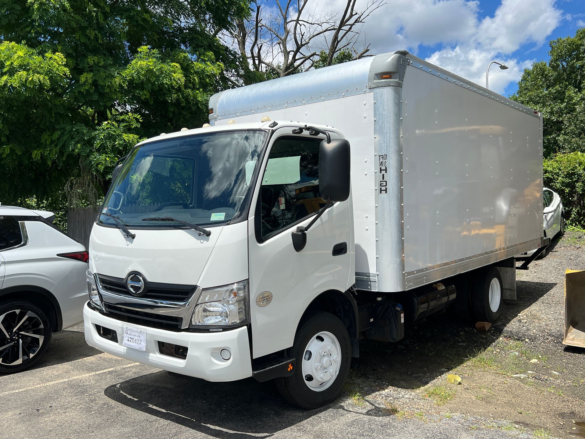 A white moving truck is parked in a parking lot next to a car.