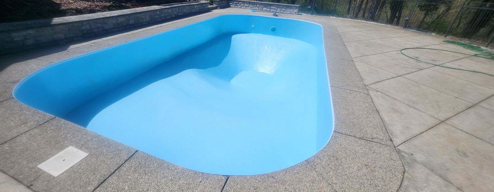 Empty blue swimming pool beside a concrete deck in bright sunlight